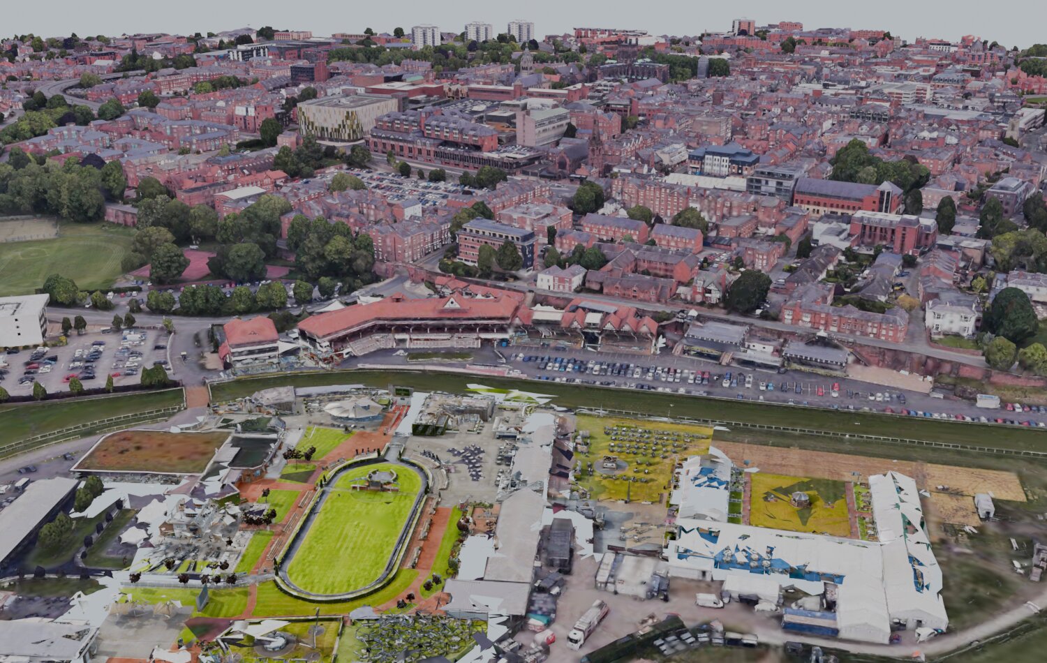 An oblique aerial view of the racecourse enclosures, where brightly coloured Matterport scan geometry of the paddock and buildings is merged into the surrounding aerial imagery of the city